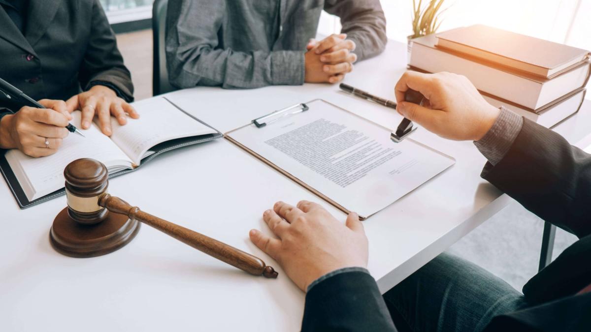 Three people at a table with legal documents, a gavel, and books, discussing paperwork.