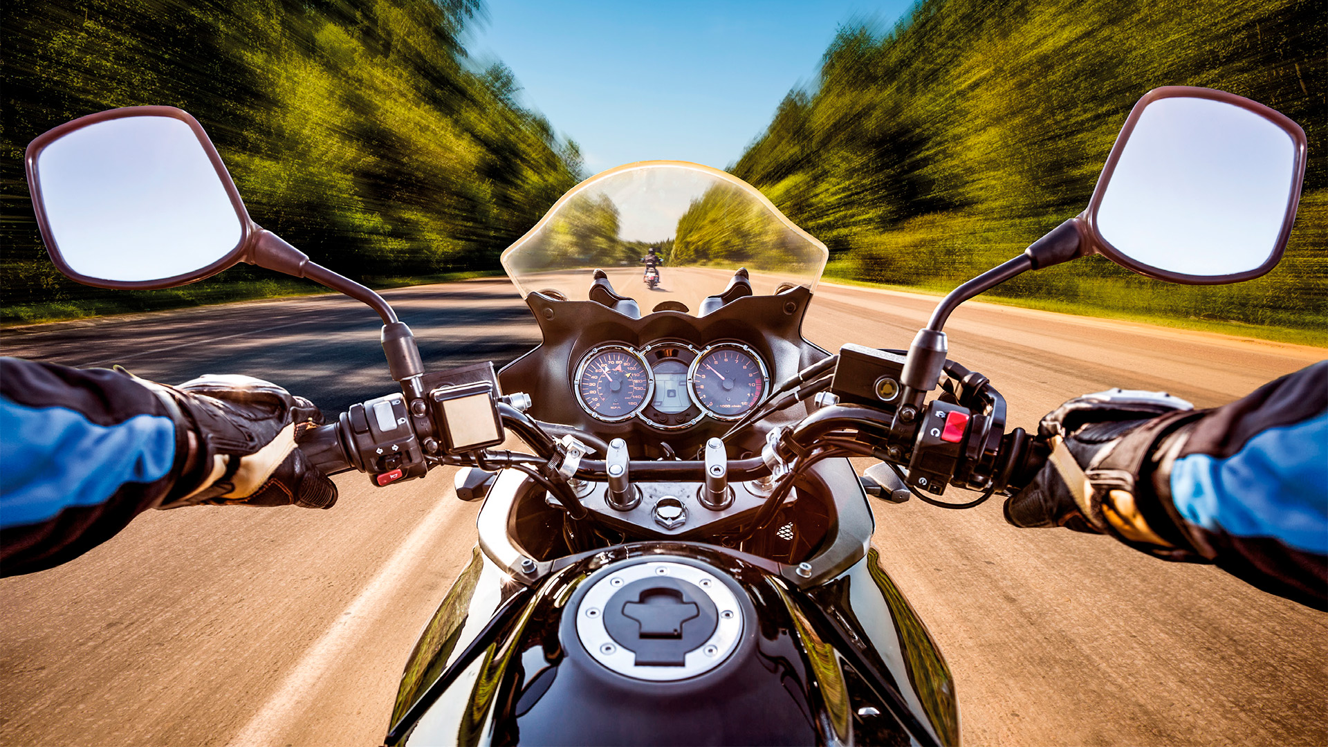 MAH-Edición-4—motocicleta Motorcyclist's view of the road, with hands on handlebars and blurred trees on both sides.