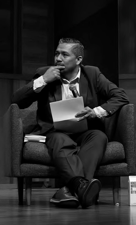 A man in a suit sits in a chair, holding papers and a pen, appearing thoughtful during an event in Estados Unidos.