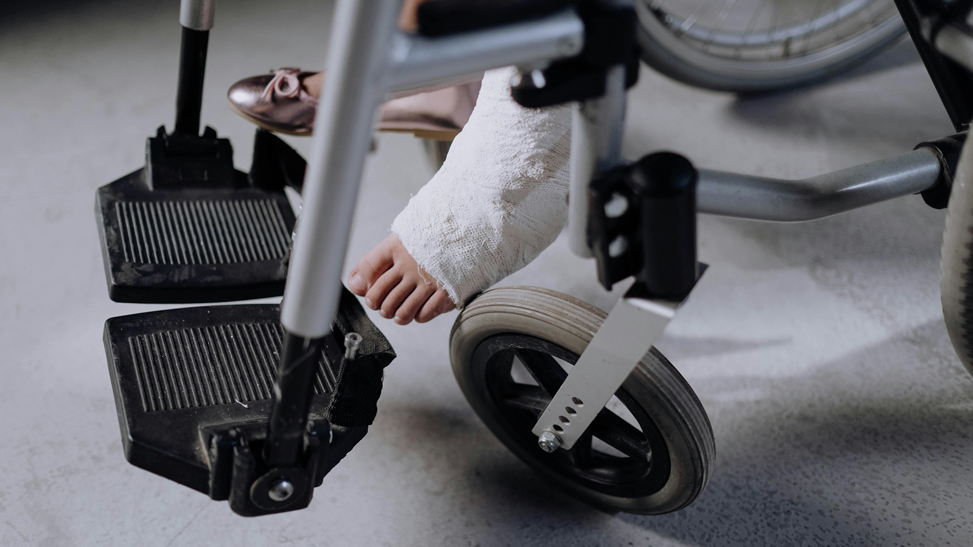 Persona-lesionada A person with a bandaged foot sits in a wheelchair, wearing a single shoe on the other foot.