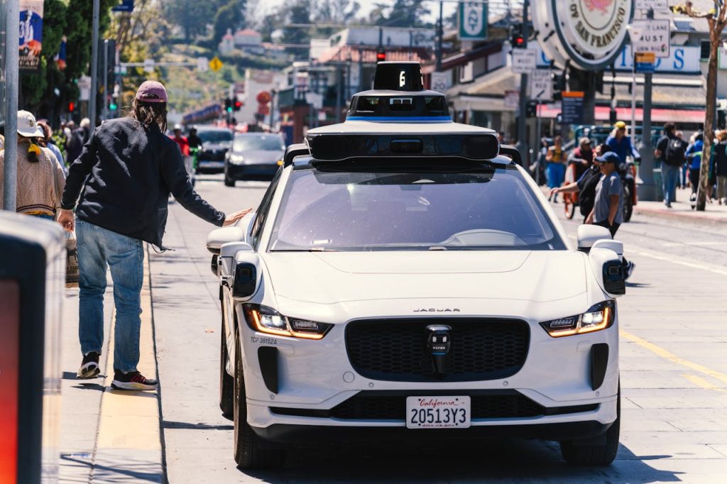 A man touches a self-driving Jaguar car with sensors on a busy city street.