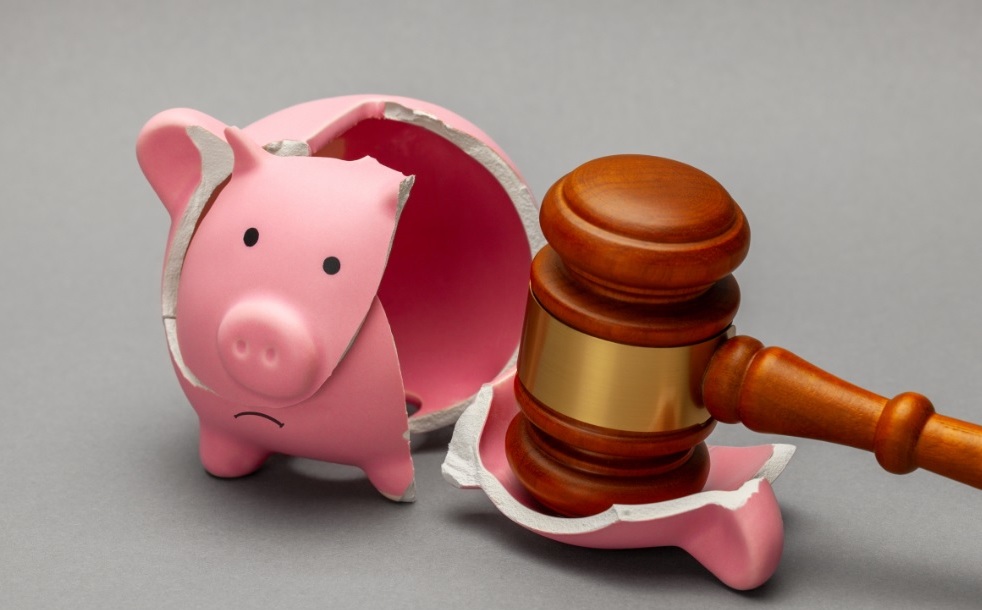 A judge’s gavel next to a sad, broken pink piggy bank on a gray background.