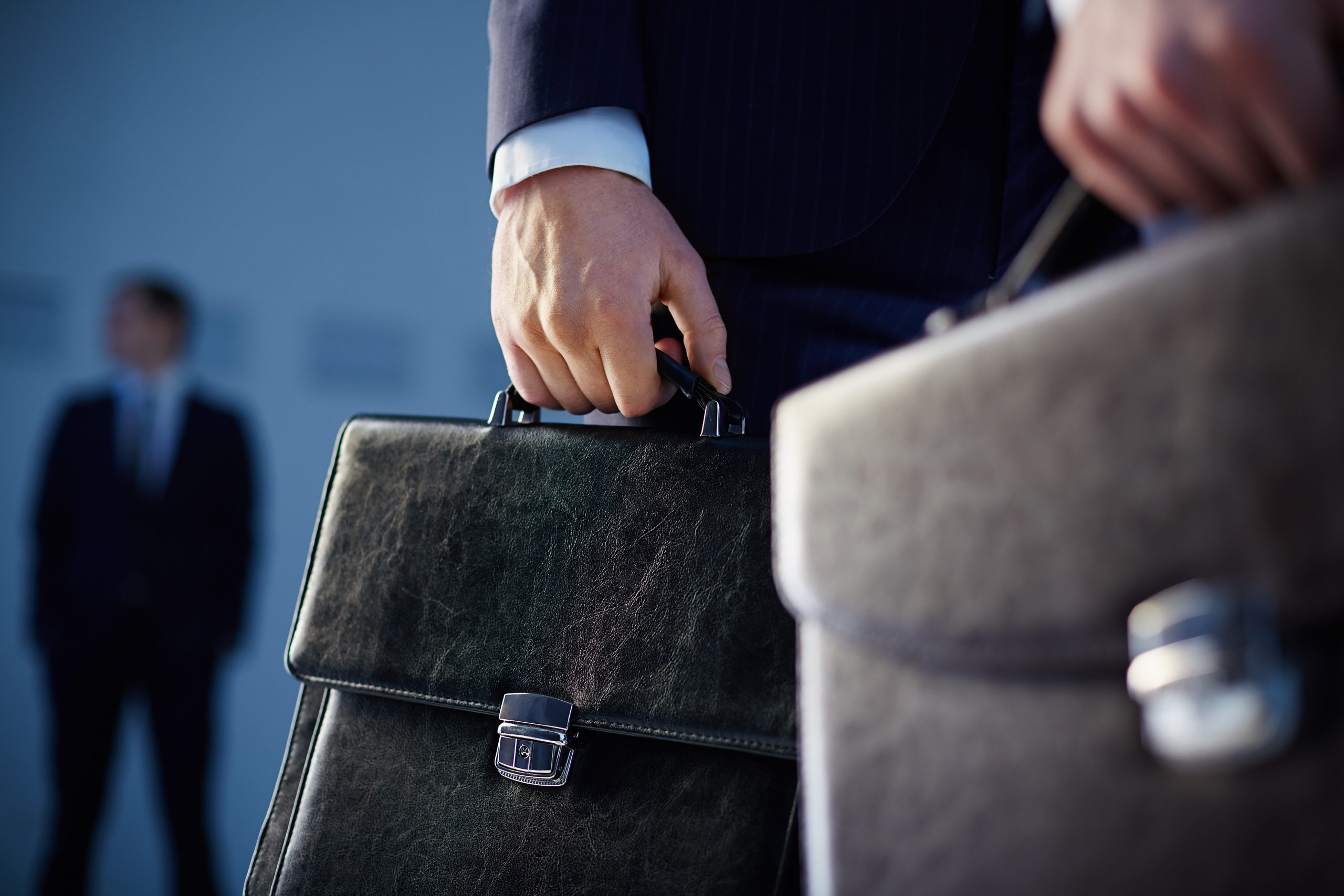 Close-up of two people in suits holding briefcases, with one person blurred in the background.