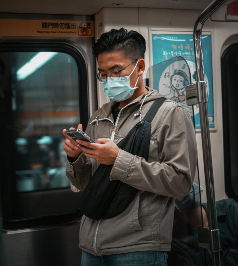Man wearing a face mask uses his phone while standing on a subway train.