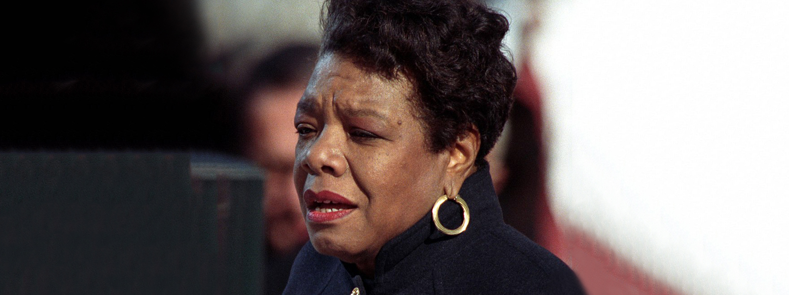maya-angelou-portada A woman with short hair and gold hoop earrings looks thoughtfully to the side, wearing a dark jacket.