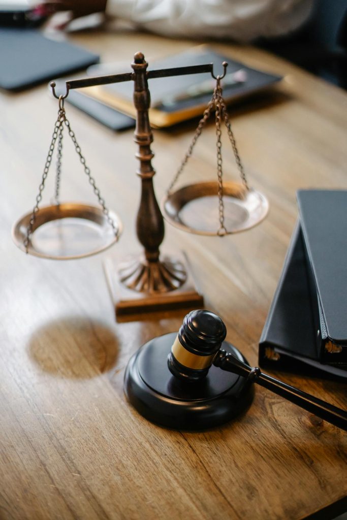 A judge's gavel and scales of justice on a wooden table with documents nearby.