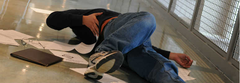 A person lying on the floor with papers scattered, appearing to have fallen in a hallway.