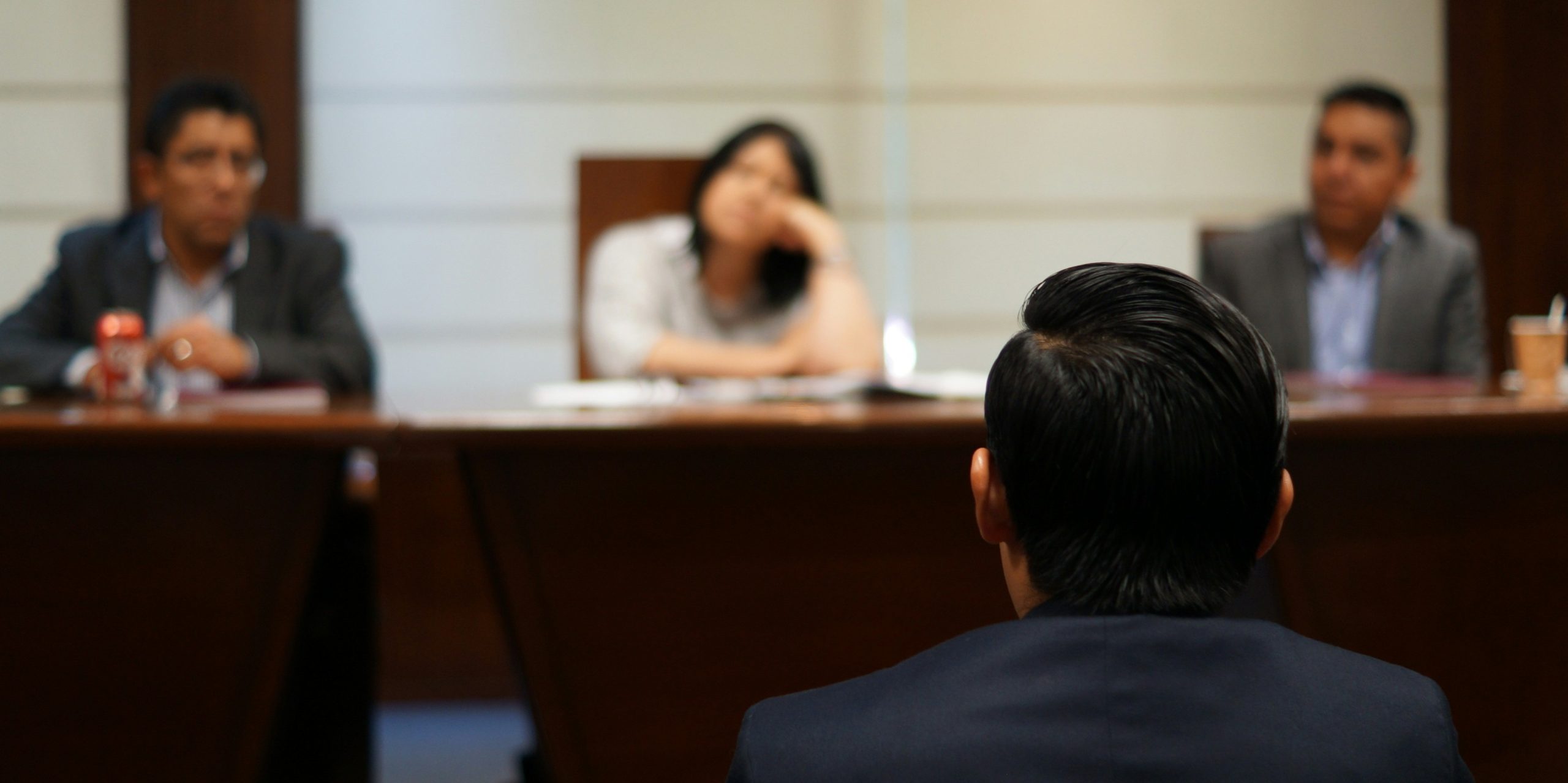 A person faces three people seated at a table, suggesting a job interview or panel discussion.