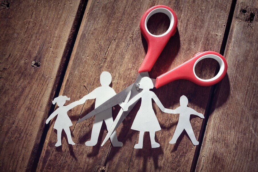 Paper cut-out family being cut by scissors with red handles on a wooden surface.