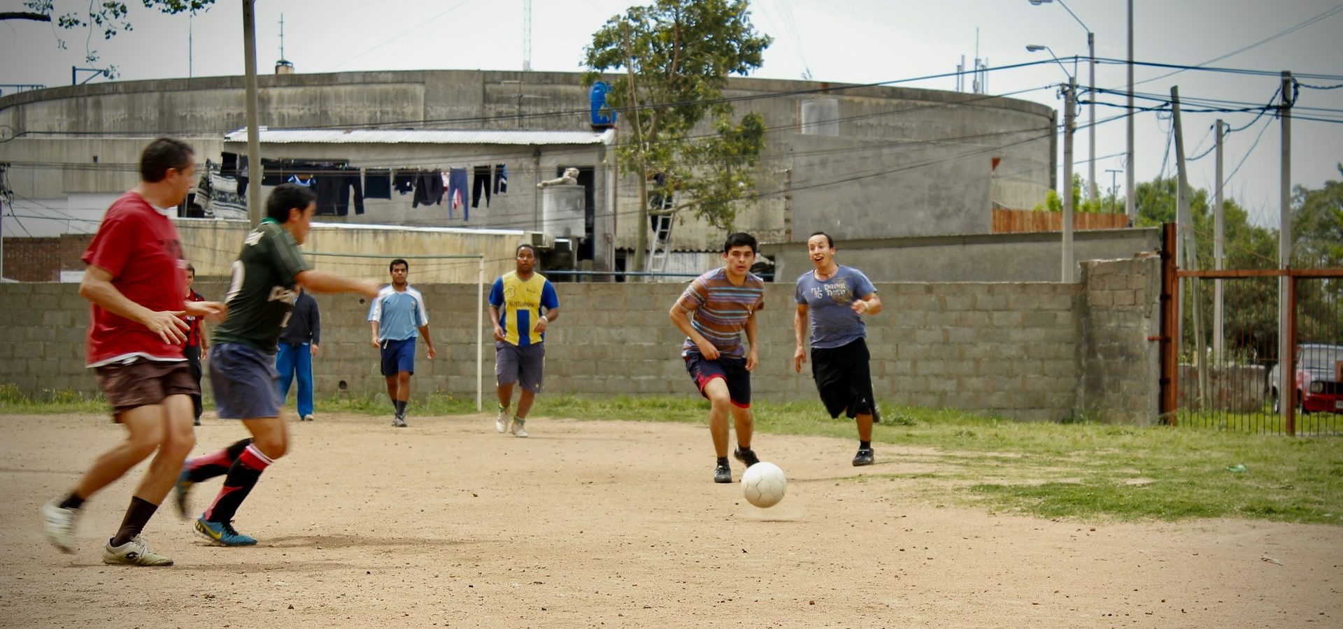 greta-scholderle-moller-xe07ZDGZ-2Q-unsplash A group of men play soccer on a dirt field in an urban neighborhood, running toward a white ball.