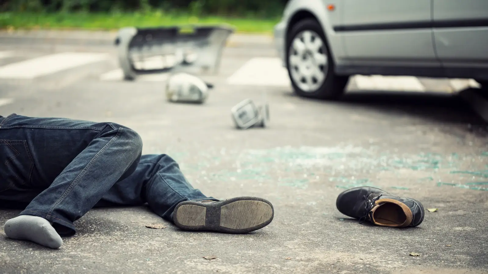 pedestrian-accidents-2 Person lying on the road after an accident near a car, with debris and a shoe scattered nearby.