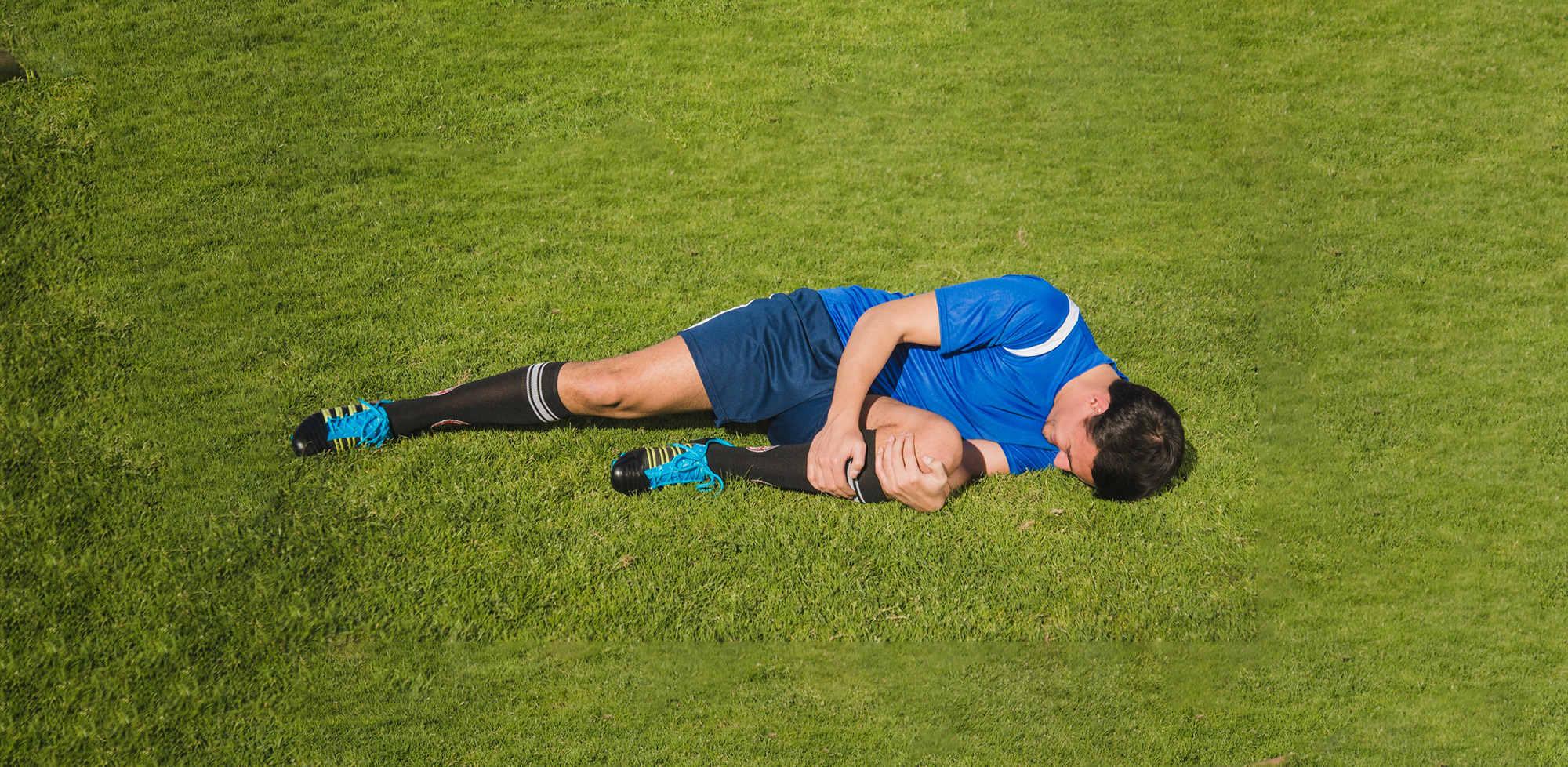 Soccer player in blue uniform lying on grass field, holding his knee in apparent pain.