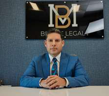 Man in a blue suit sits at a desk with a "BM Brave Legal" sign on the wall behind him.