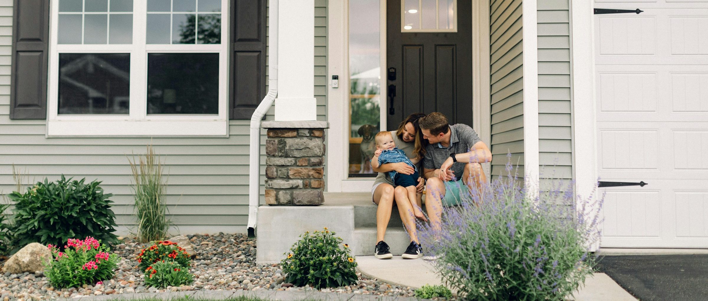 A family sits on the front steps of their house, with the father kissing the child on the cheek.
