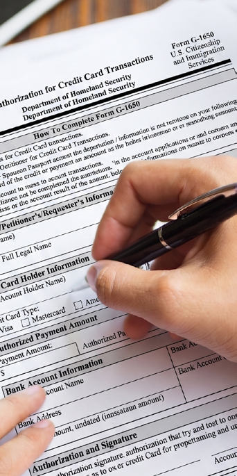 A hand fills out a Department of Homeland Security credit card authorization form with a pen.