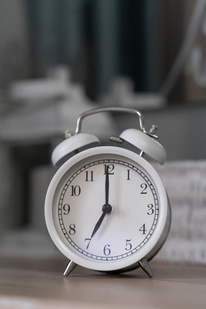A white analog alarm clock set to seven o’clock.