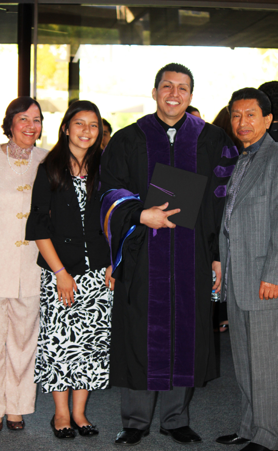 A graduate in a cap and gown stands with three family members.