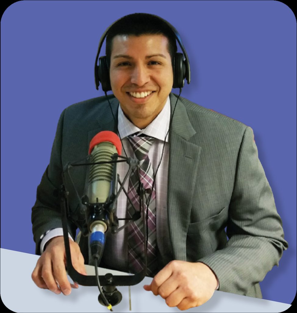 A smiling man in a suit and headphones sitting in front of a professional microphone.