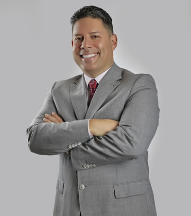 A smiling man in a grey suit with arms crossed.