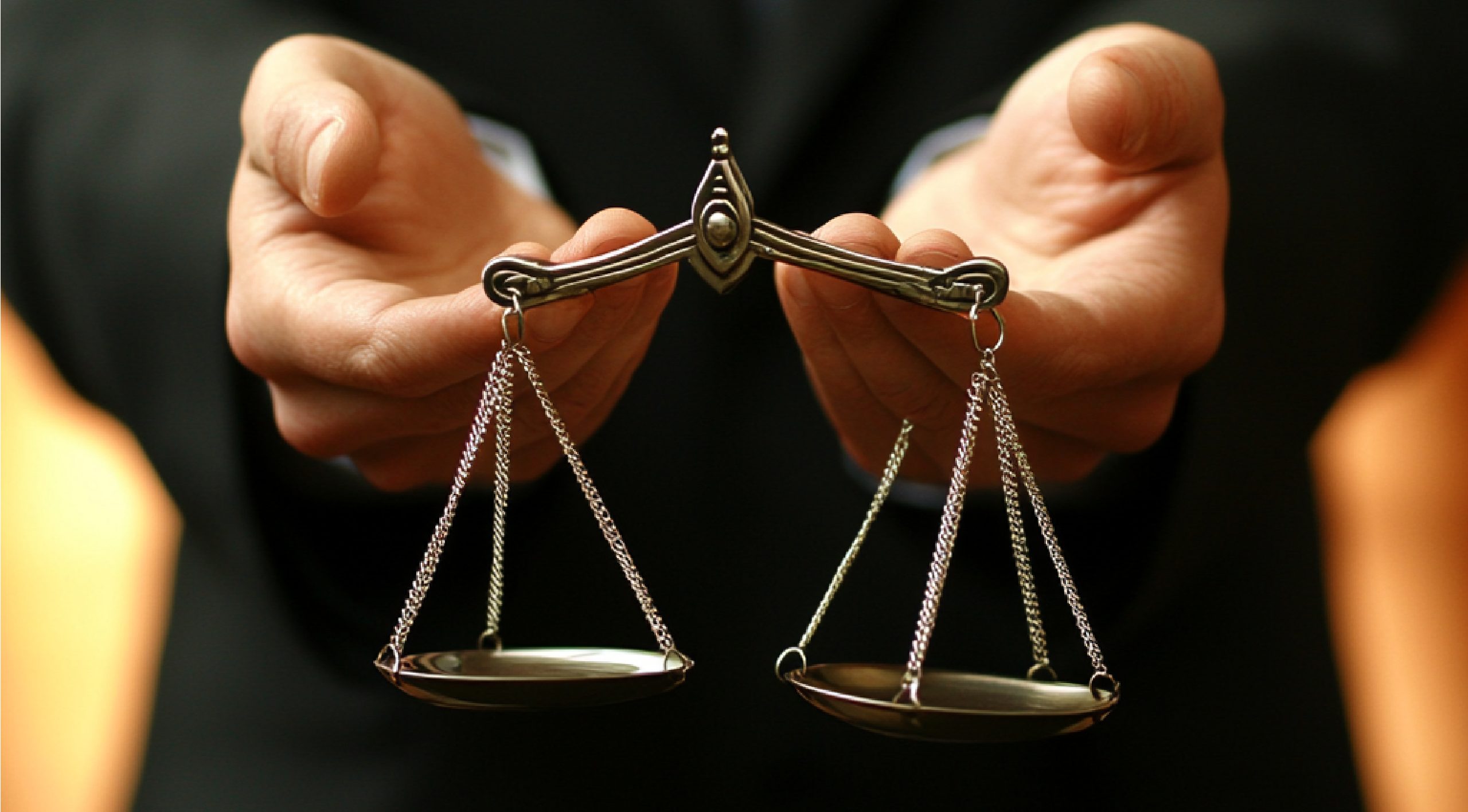 A person in a suit holding a small metal scale of justice.